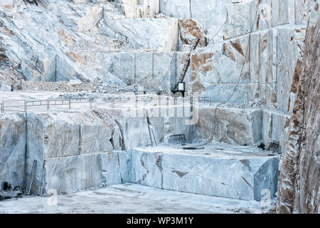 Open cast mine pit with white Carrara marble being cut into rectangular blocks for the construction industry and sculptures in Tuscany, Italy Stock Photo