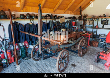 View into an old fire station with hand-operated fire trucks, old uniforms lined up on the walls and various fire fighting equipment. Stock Photo