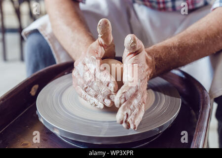Man potter working on potters wheel making ceramic pot from clay in pottery workshop. Stock Photo