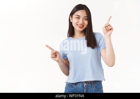 Lively excited happy smiling pretty brunette asian girl enthusiastic joyful mood dancing cute toothy grin pointing sideways up left index fingers show Stock Photo