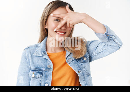 Silly optimistic lucky asian blond girl show peace victory gesture fool around playful positive mood make gesture face look one eye camera smiling bro Stock Photo