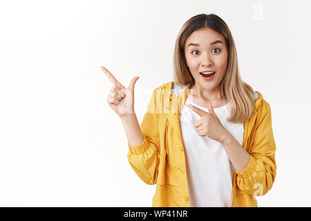 Enthusiastic curious charming happy asian talkative girl pointing upper left corner index fingers intrigued talking awesome product discuss excited ad Stock Photo