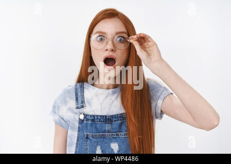 Omg no way. Impressed gasping redhead girlfriend drop jaw touch glasses astonished, pop eyes camera amazed look wondered and shook, listen fresh rumor Stock Photo