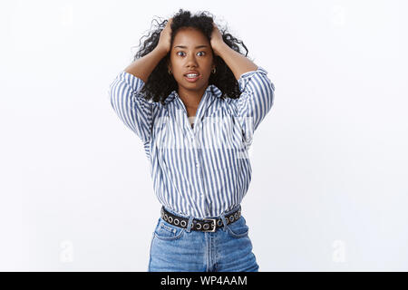 Intense african american curly-haired woman panic holding hair widen eyes gasping shocked made huge mistake standing stupor terrified stunned terrible Stock Photo