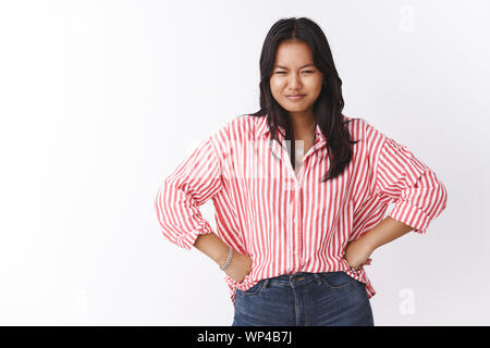 Girl squint feeling suspicious as staring at camera, holding hands on waist in bossy pose smirking expressing disbelief having doubts as trying unders Stock Photo