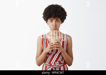 Always sad when coffee ends. Displeased and upset cute dark-skinned female in striped overalls, pursing lips and making miserable begging expression, Stock Photo