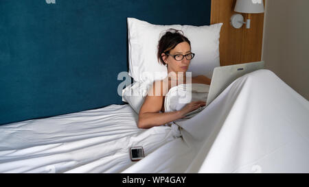 A woman working on her computer whilst in bed. Stock Photo
