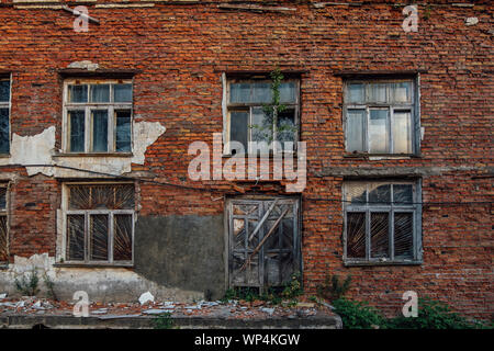 Old grungy wall of red brick with broken windows and wooden door. Stock Photo