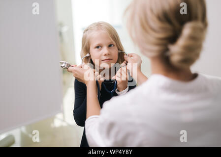 Cute funny kid girl wears a stethoscope under supervision of pediatrician Stock Photo
