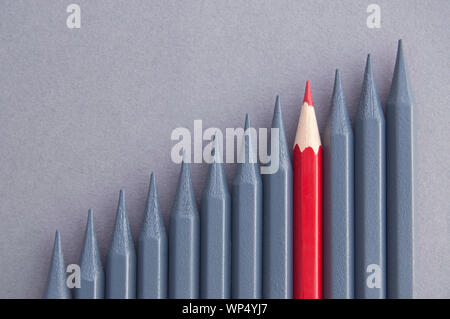 Red pencil in the middle standing out amongst greyed out pencils Stock Photo