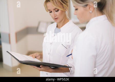 Two women doctors standing with clipboard at hospital and discussing cases Stock Photo
