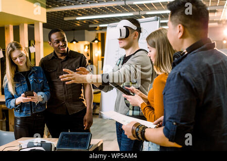 Business team of young multiethnical people presenting new project to a client on a virtual reality simulator. Young Caucasian man the client with VR Stock Photo