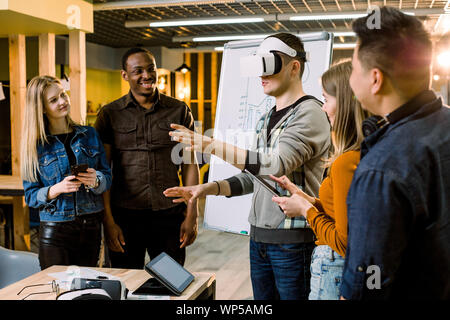 Business team of young multiethnical people presenting new project to a client on a virtual reality simulator. Young Caucasian man the client with VR Stock Photo