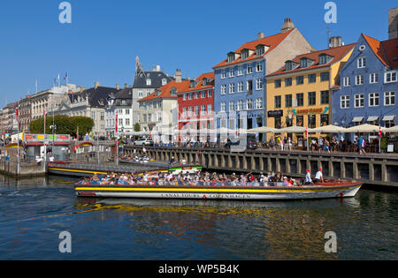 Canal cruise boat starting tour from the end of Nyhavn Canal at Kongens Nytorv moving alon the beautiful brightly coloured old houses along the canal. Stock Photo