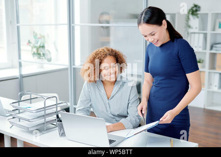 One of female managers pointing at financial paper while showing it to colleague Stock Photo