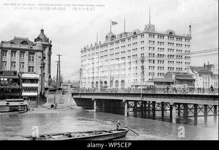 [ 1920s Japan - Oebashi Bridge in Osaka ] —   Oebashi Bridge over the Dojima River in Osaka.  The large building is the Dojima Building, constructed in 1923 (Taisho 12) by Takenaka Komuten. The building with the dome housed Fukutoku Seimen Hoken (福徳生命保険). It was designed by Kingo Tatsuno (辰野金吾, 1854-1919) and Yasushi Kataoka (片岡安, 1876-1946) and opened in 1919 (Taisho 8).  The steel bridge on this photo was built in 1910 (Meiji 43). Construction of the current stone bridge was started in 1930 (Showa 5).  This effectively dates this photo to the 1920s.  20th century vintage postcard. Stock Photo