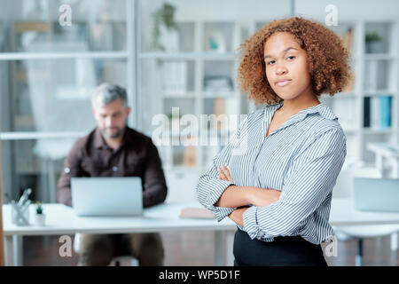 Young confident office manager with curly hair crossing arms on chest by camera Stock Photo