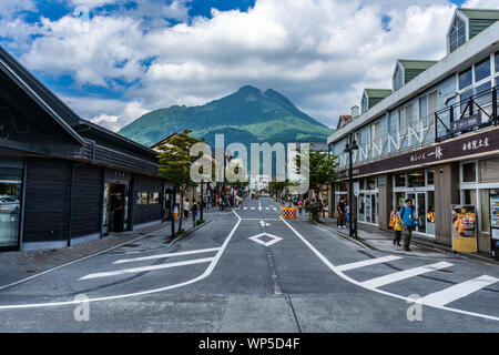 Yufuin, Japan - 12 July 2019 - Tourists walk along the main road from the train station in Yufuin, Japan toward shopping and business area with view o Stock Photo