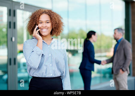 Young cheerful employee looking at you while calling on smartphone Stock Photo