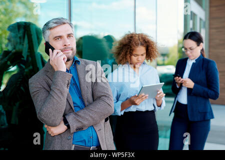Serious businessman talking on smartphone while standing by office building Stock Photo