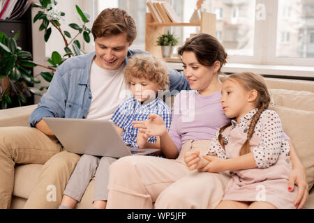 Contemporary couple and two kids discussing movie while watching it at leisure Stock Photo