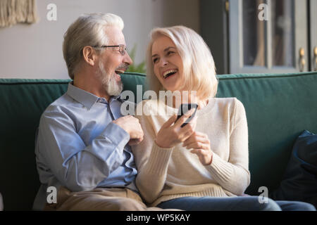 Happy retirees family laughing using smartphone at home. Stock Photo