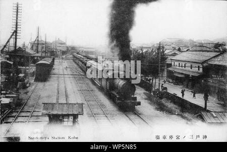 [ 1910s Japan - Japanese Steam Locomotive in Kobe ] —   A steam locomotive pulling passenger cars leaves Sannomiya Station, seen in the back, in Kobe, Hyogo Prefecture on the way to Osaka.  The railroad connection between Kobe and Osaka was opened in May 1874.  Sannomiya Station is still in its old location in this photo. It was moved to its current location on October 10, 1931. The old Sannomiya Station was reopened in 1934 as Motomachi Station.  20th century vintage postcard. Stock Photo