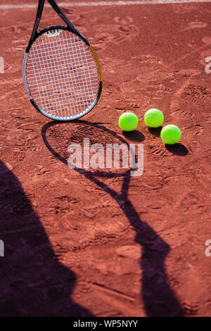 Still life of tennis balls and the shadow of a rman holding a tennis racquet on a red clay tennis court. Stock Photo