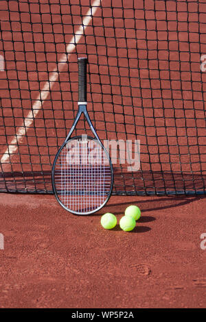 Still life of tennis balls and a racket on a red clay tennis court. Stock Photo