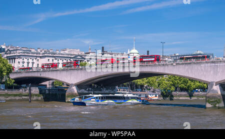 Waterloo Bridge during rush hour on clear spring day; several Double Decker buses appear on top of the bridge and recreational boat moving under it Stock Photo