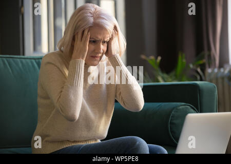 Frustrated elderly woman confused by laptop breakdown problems Stock Photo