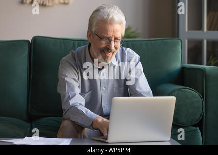 Smiling elderly man using laptop browsing internet at home Stock Photo