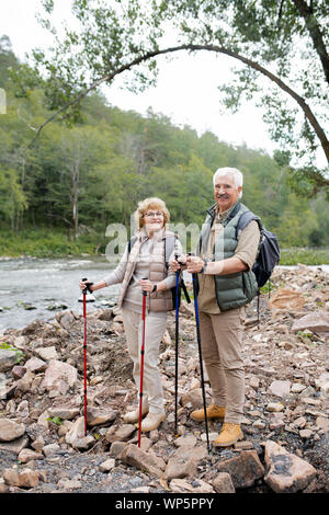 Happy mature man and woman with trekking sticks standing on stones Stock Photo