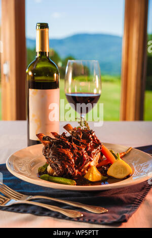 Beef spare ribs on a white plate with a bottle of red wine in the background.