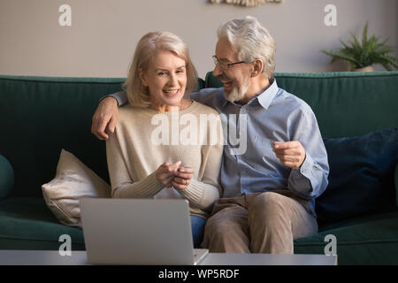Smiling elderly spouses use laptop watching movie online Stock Photo