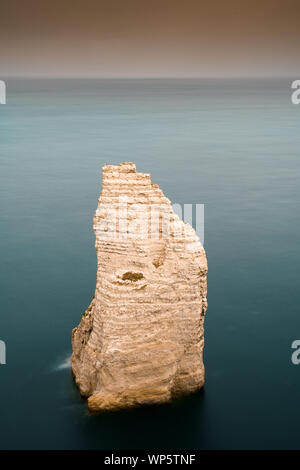 A vertical view of a rock needle granite cliff in a calm dark blue ocean Stock Photo