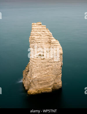 A vertical view of a rock needle granite cliff in a calm dark blue ocean Stock Photo