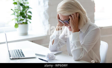 Tired aged businesswoman feel fatigue suffering from headache Stock Photo