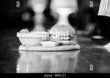 Fast food concept. Burger with cheese meat and salad. Cheat meal. Delicious burger with sesame seeds. Burger menu. High calorie snack. Hamburger and french fries and tomato sauce on wooden board. Stock Photo