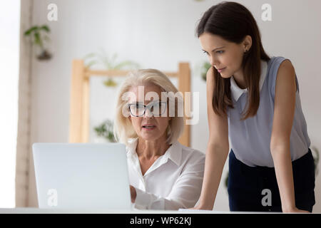 Female colleagues talk sharing ideas working on laptop Stock Photo