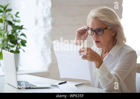 Confused senior businesswoman surprised reading paper letter Stock Photo