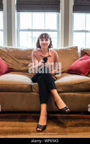 Young woman sitting on a couch in business attire watching television. Stock Photo