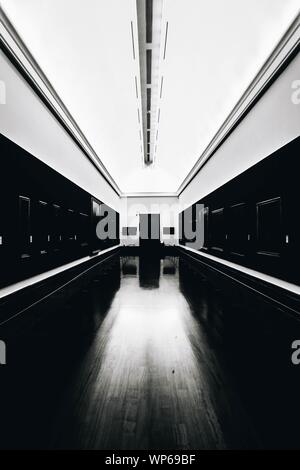 Vertical grayscale shot of an empty museum with empty frames on dark walls and illuminated ceiling Stock Photo