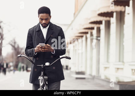 Man in suit texting on phone, standing with bike on street Stock Photo