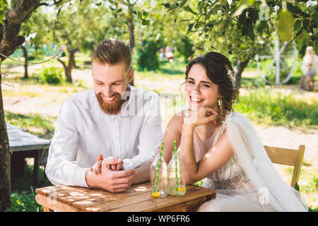 Attractive couple newlyweds, happy and joyful moment. bride and groom sit at table set for two in woods. Concept romantic date. Wedding couple sitting Stock Photo