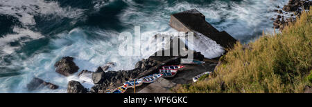 A wild sea hitting the scenic Porto Pesqueiro/fishing port of Arnel with its colorful fishing boats. Near Nordeste, on the eastcoast of the Azores isl Stock Photo