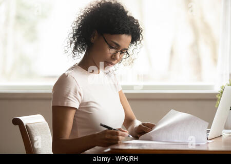 Focused biracial woman in glasses study correct paperwork Stock Photo
