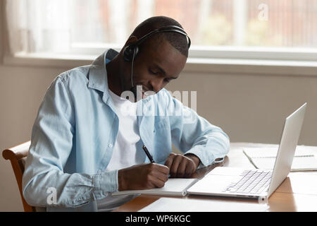 Focused biracial man in headset writing studying at laptop Stock Photo