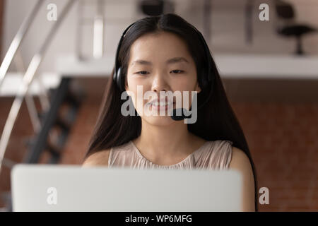 Close up happy asian woman wearing headphones, consulting client online. Stock Photo