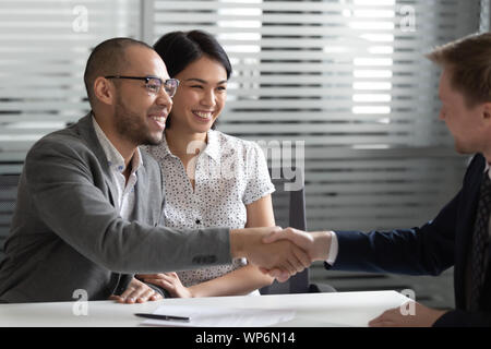 Cheerful mixed race married spouse shaking hands with real estate agent. Stock Photo